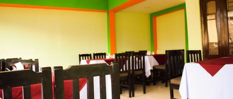A dining area with tables and chairs, green and orange walls, and a wooden door.