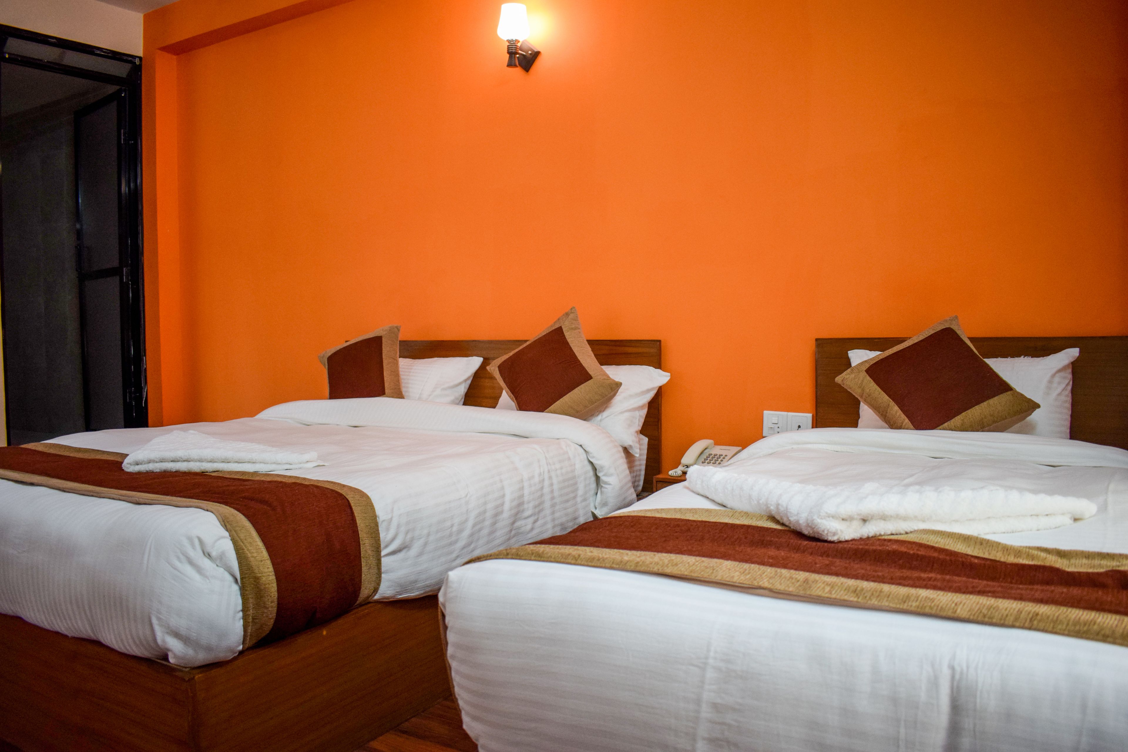 A hotel room with two beds, each with white bedding and brown accents, and an orange wall.