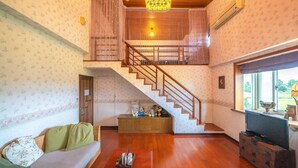 Uma sala de estar espaçosa com escada de madeira, um sofá, uma televisão e uma janela grande.