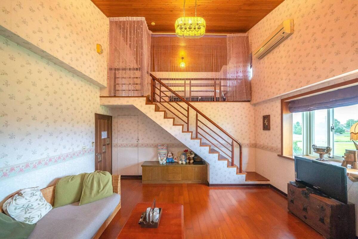 A spacious living room with a wooden staircase, a sofa, a television, and a large window.