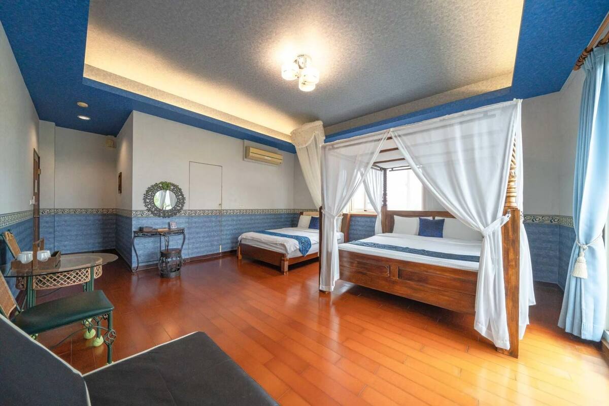 A room with a wooden floor, a bed with a canopy, a small table with chairs, and a decorative mirror on the wall.