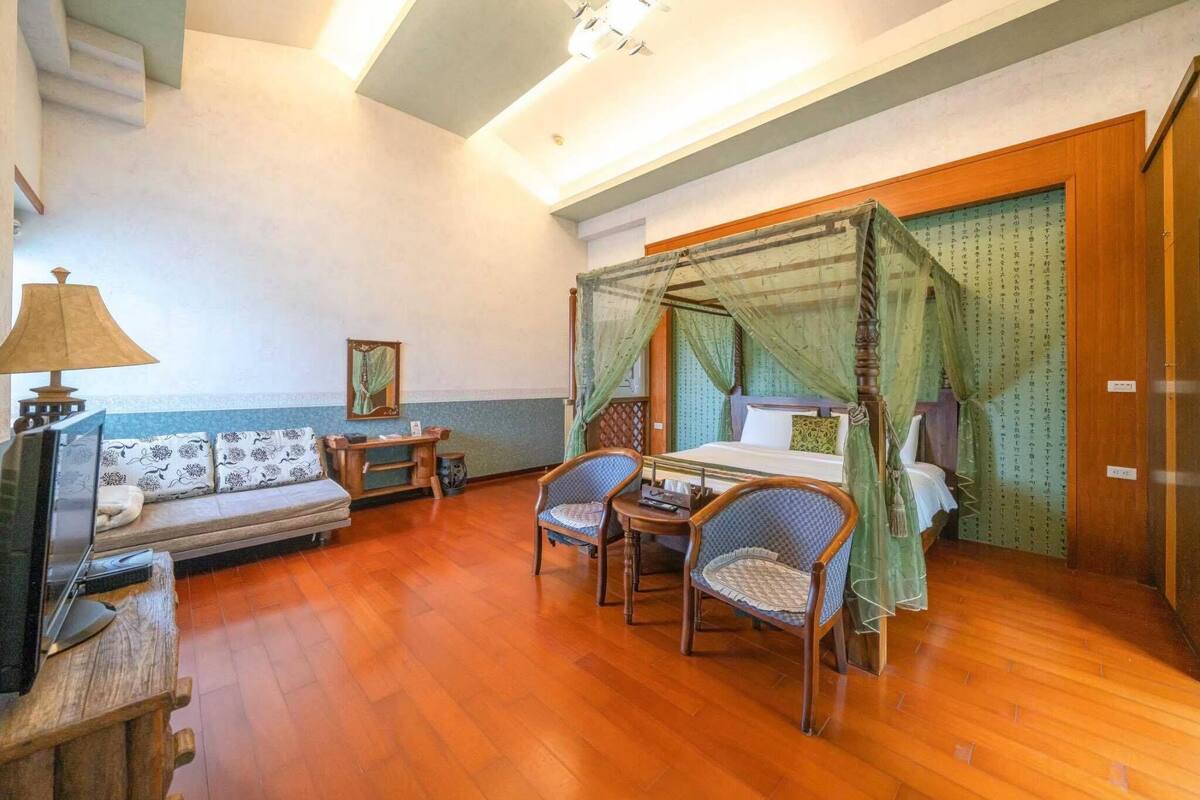 A room with a bed, a sofa, two chairs, a small table, and a television.