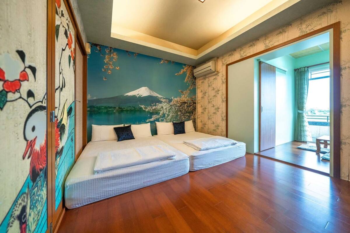 A room with two beds, a mural of Mount Fuji, and a view of a balcony.