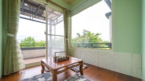 Quarto com mesa de madeira, almofadas e vista para o verde lá fora.