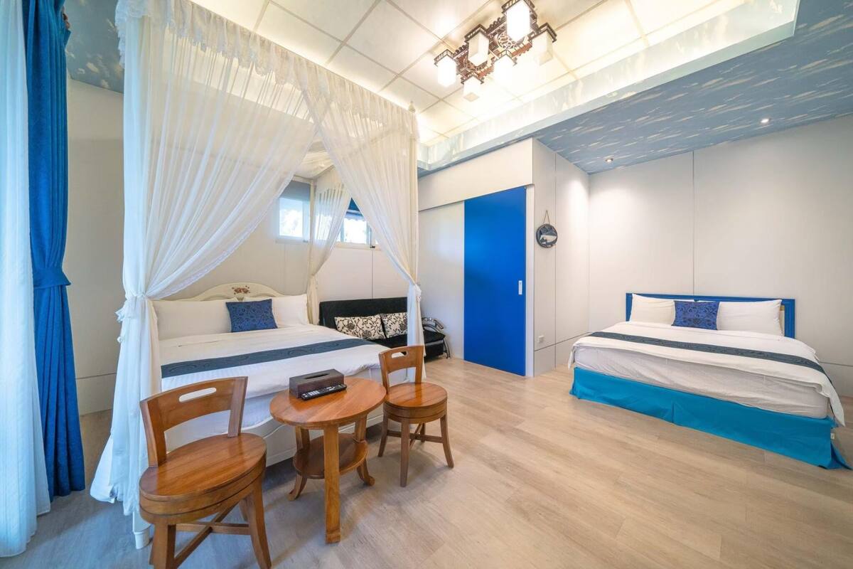 A bedroom with two beds, a small table with chairs, and a canopy bed.