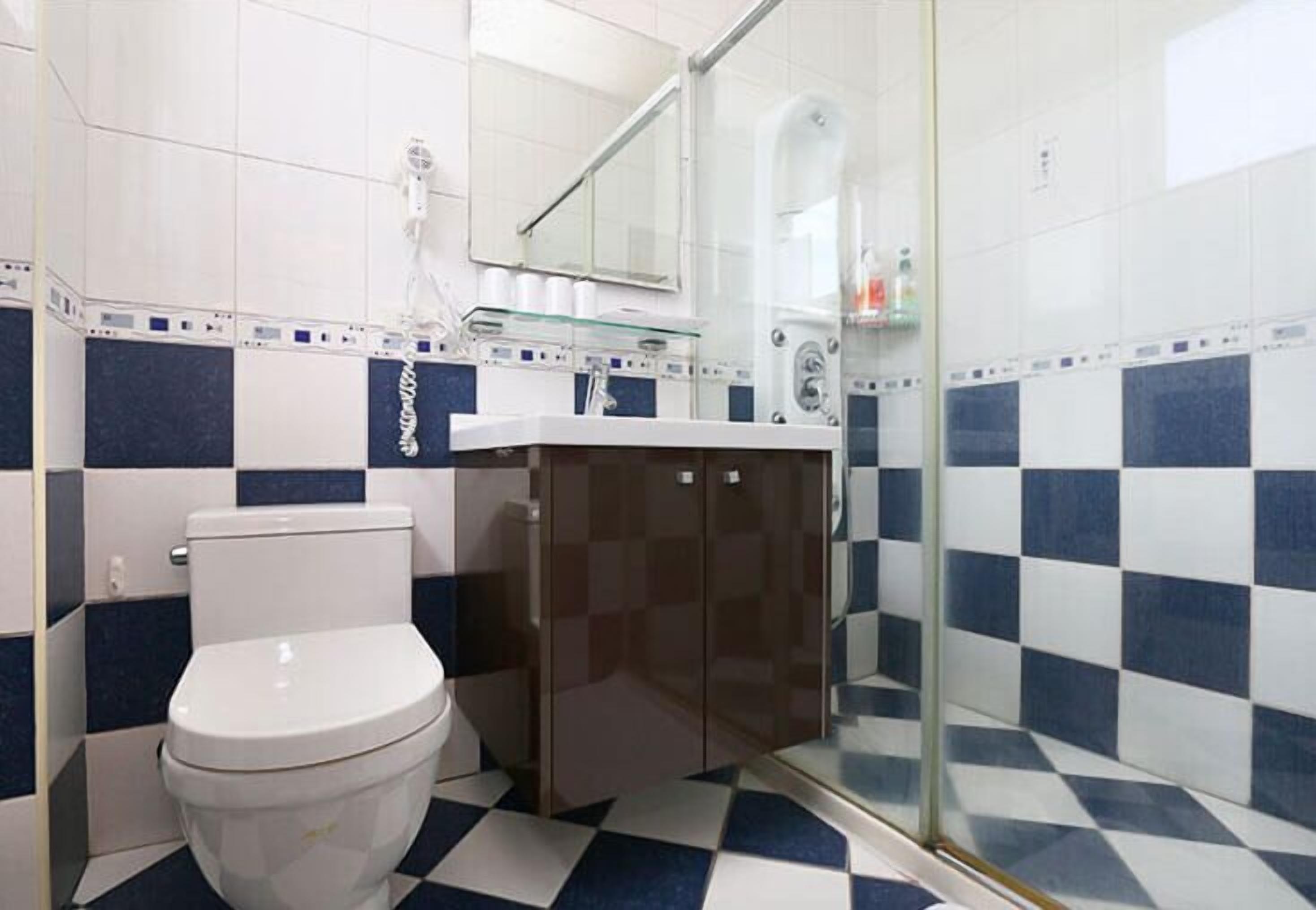 Un baño con inodoro blanco, cabina de ducha de vidrio y lavamanos con espejo.