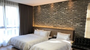 Habitación de hotel con dos camas, un revestimiento de ladrillo, suelo de madera y un sofá de cuero negro.