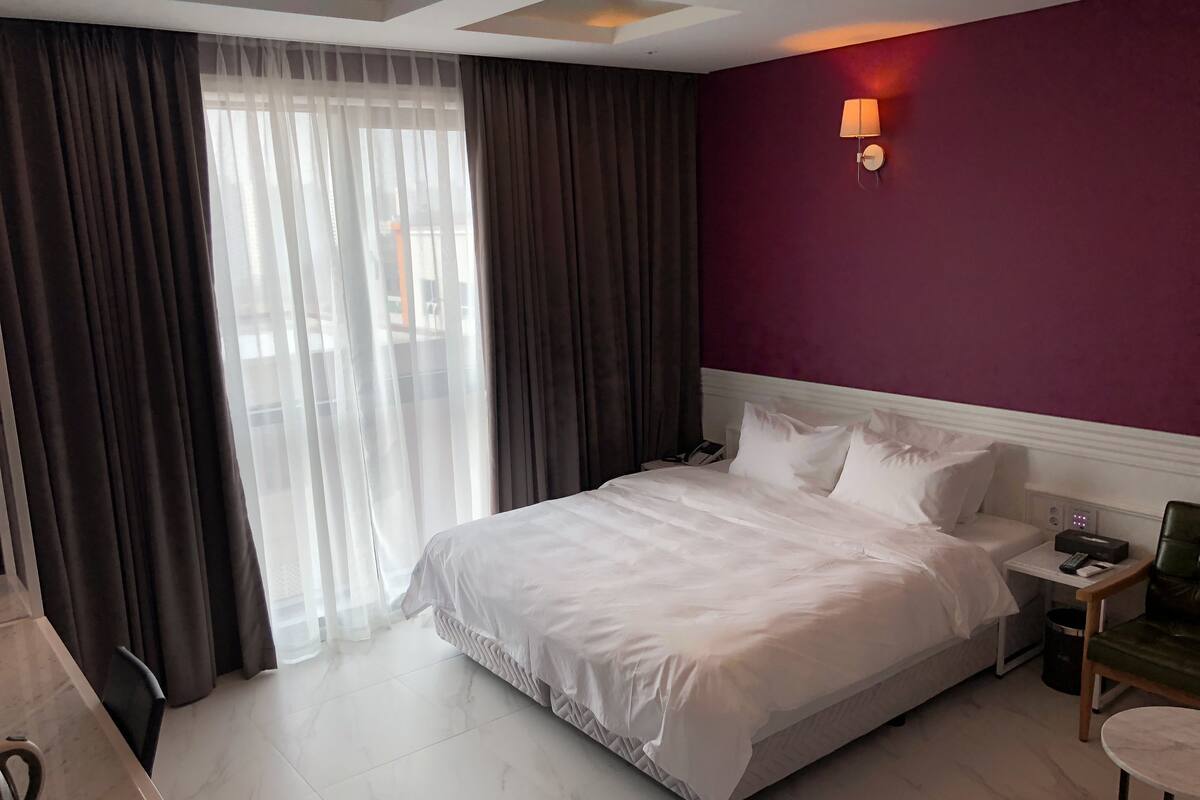 A hotel room with a large bed, a nightstand, a desk, and a chair.