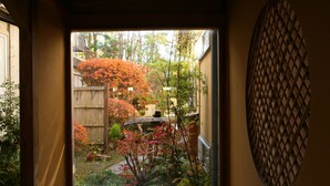A view through a window of a garden with a wooden fence, various plants, and a stone pathway. - Yudanaka Yumoto (Yamanouchi)