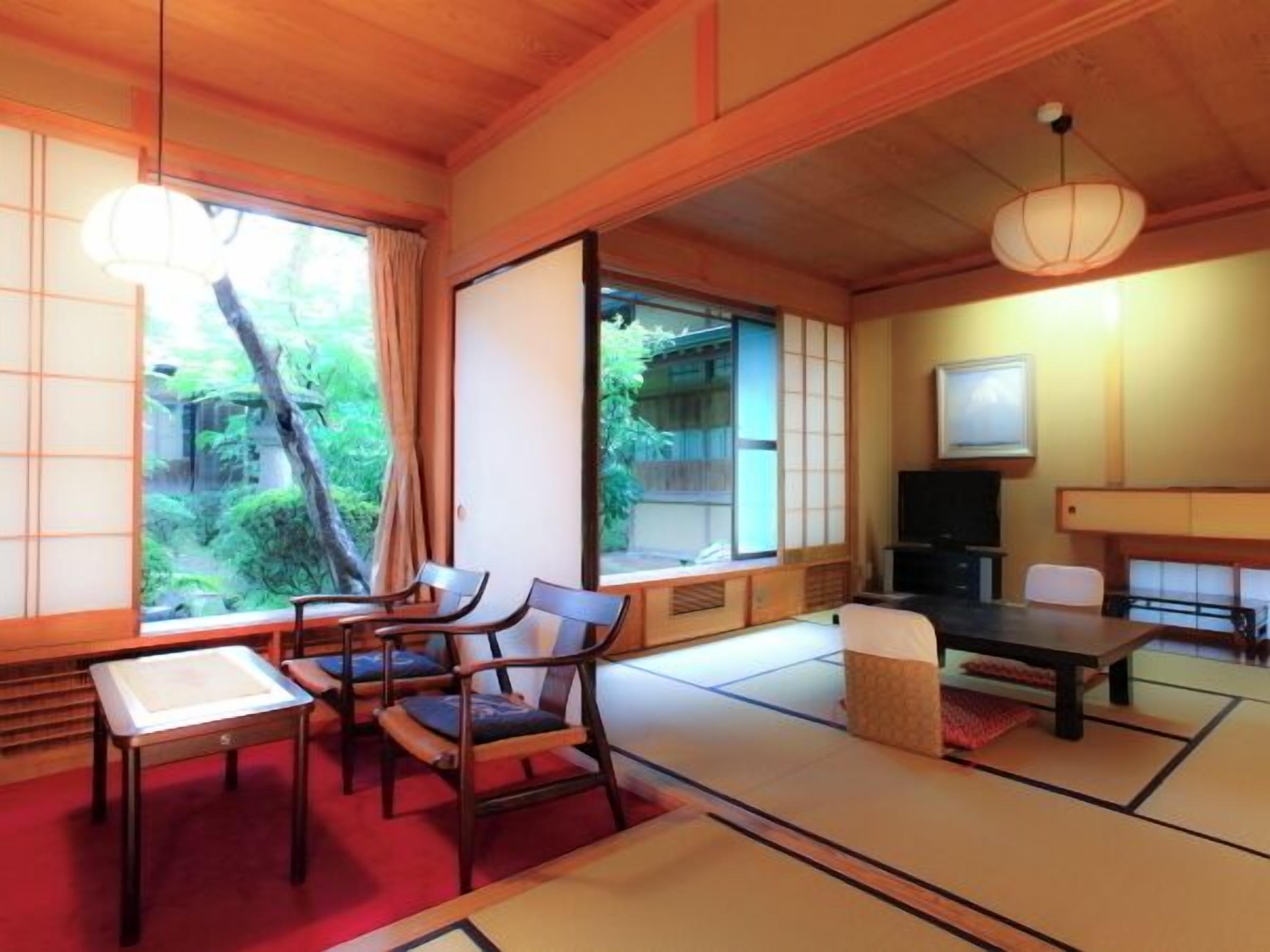 A traditional Japanese room with tatami flooring, a low table, chairs, a TV, and sliding doors.