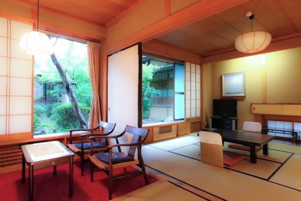 A traditional Japanese room with tatami flooring, a low table, chairs, a TV, and sliding doors.