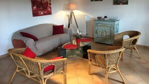 Una sala de estar con un sofá, dos sillones de mimbre, una mesa de centro de vidrio, una lámpara y un aparador con diseños florales.