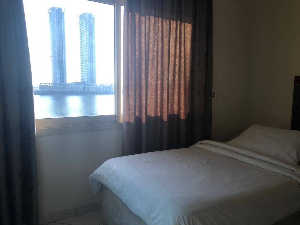 A hotel room with a bed, curtains, and a window with a view of tall buildings.