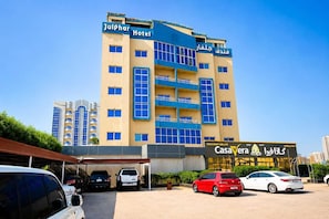 A hotel with multiple floors, balconies, and a parking area with several cars. - Julphar Hotel (Ras Al Khaimah)