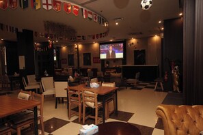 A hotel lobby with a checkered floor, wooden furniture, a television screen, and flags on the wall.