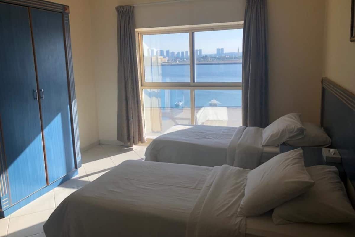 A hotel room with two beds, a large window with a city view, and a wardrobe.
