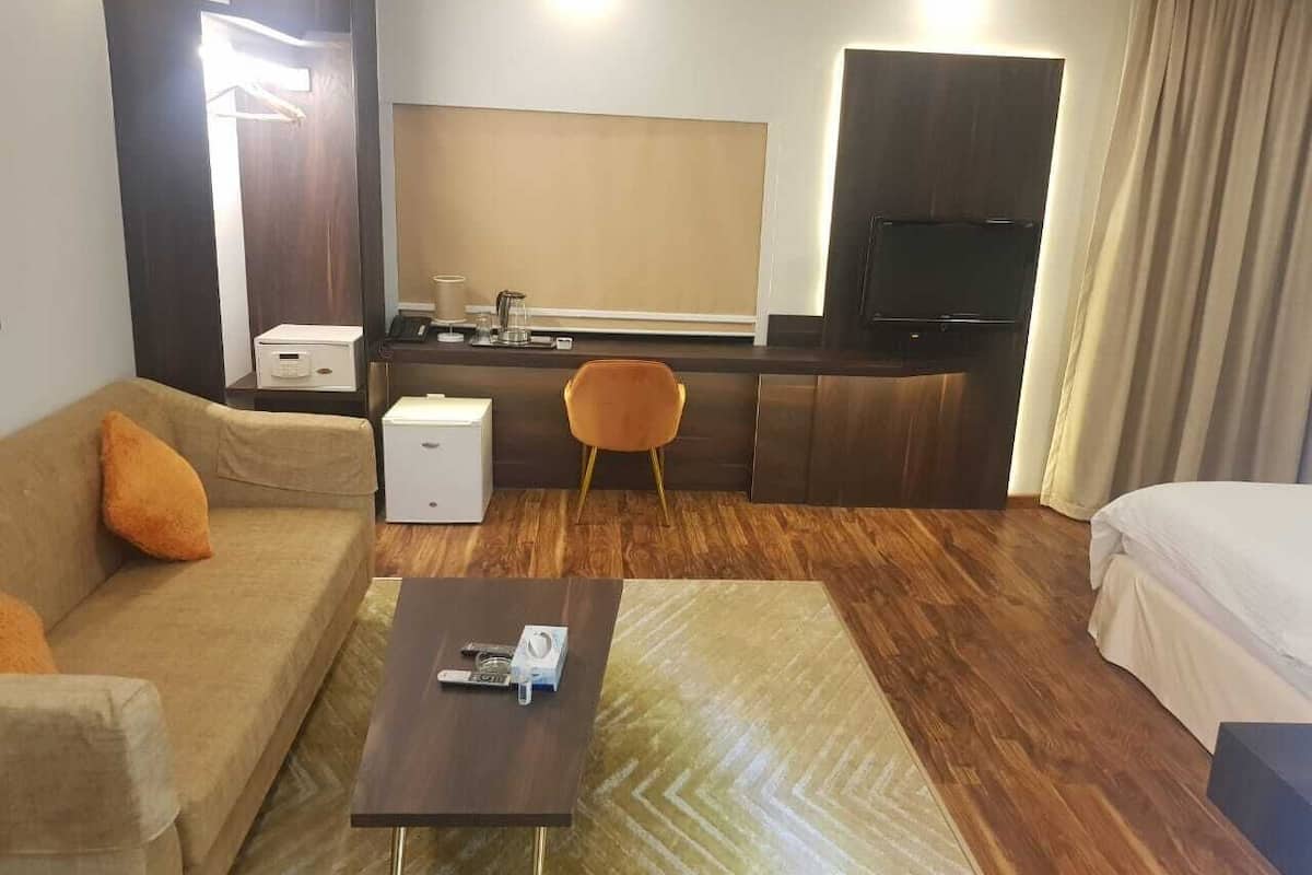 A hotel room with a sofa, a coffee table, a TV, a bed, and a small kitchenette area.