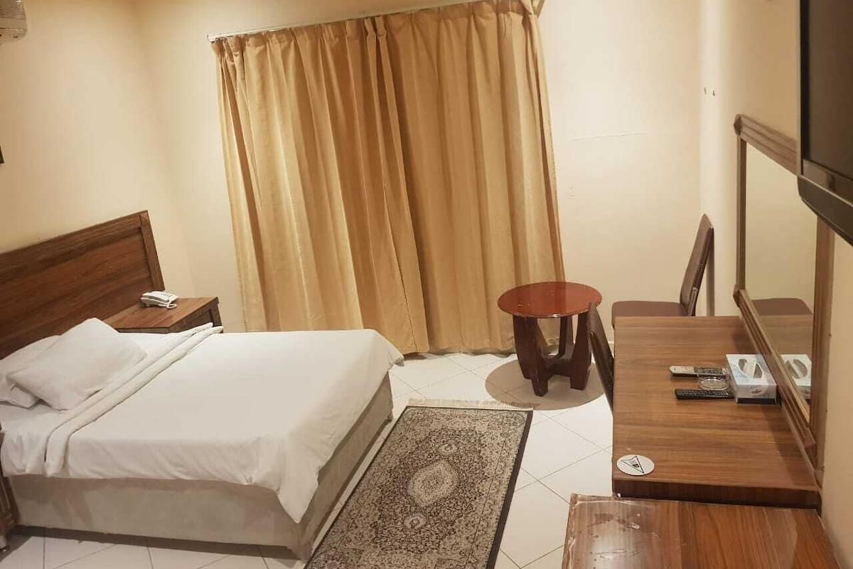 A hotel room with a bed, a small round table, a chair, a TV, and a window with curtains.