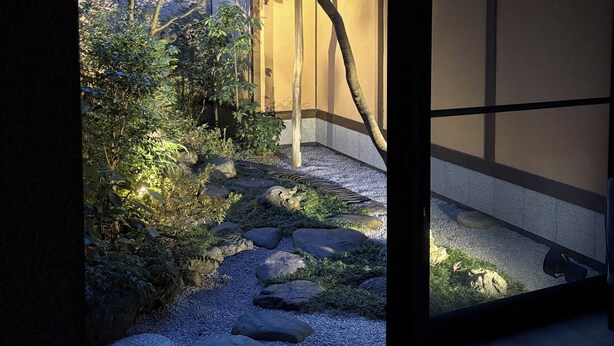 Um jardim japonês tradicional com um caminho de cascalho, pedras e vegetação.