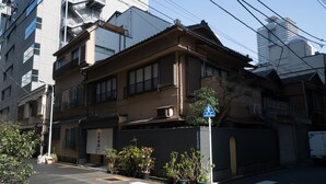 A traditional Japanese building with a crosswalk in front, surrounded by potted plants and a clear blue sky. - Ito Ryokan (Tokyo)