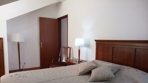 A bedroom with a bed, two bedside lamps, a wooden chair, and a door. - Janelas da Praia, Apartment by the beach. (Praia da Vitória)