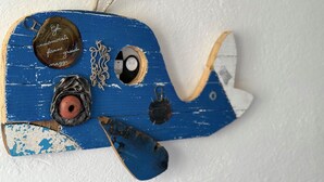 Une décoration en forme d’avion, aux couleurs bleu et blanc, d’un style rétro, avec une petite hélice et un emblème circulaire portant une inscription.