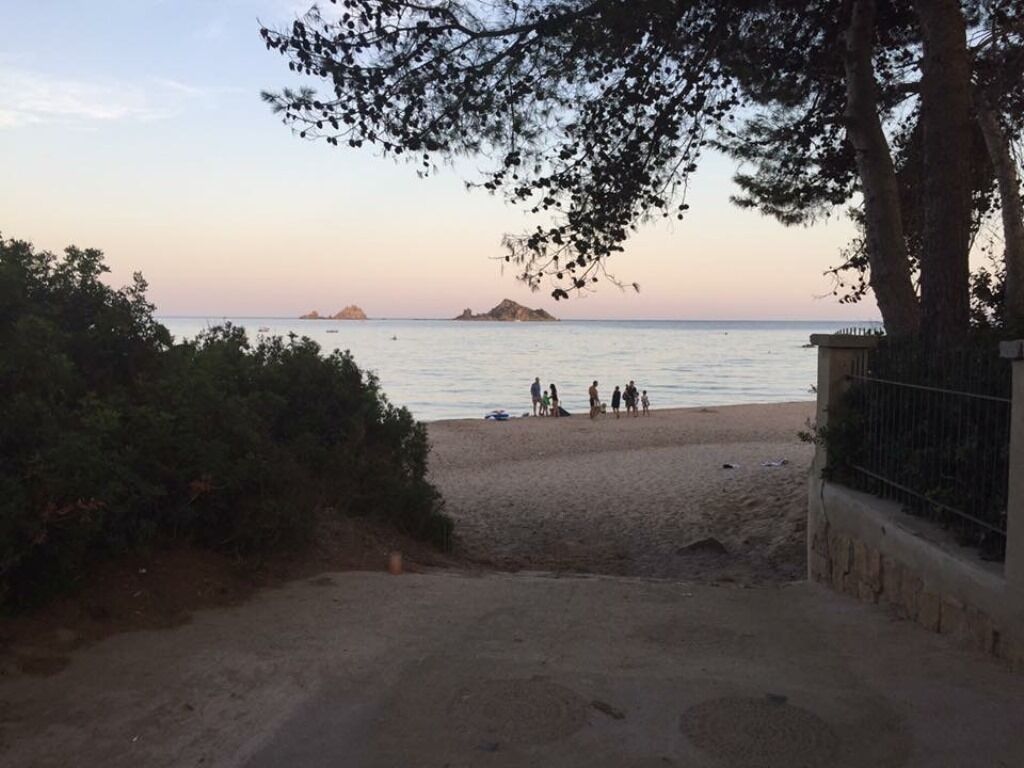 A beach with a dirt path leading to the water, a group of people on the sand, and a distant island.