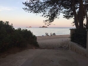 Una platja amb un camí de terra que condueix a l'aigua, un grup de persones a la sorra i una illa a la distància.