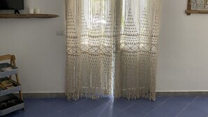 A room with a large window covered by a decorative curtain, a television on a stand, and a shelf with items. - Apartment 20 meters from the sea (Tancau sul mare)