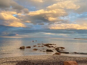 Una platja amb roques disperses i un moll allunyat.
