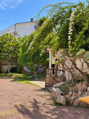 Een tuin met een grindpad, een pergola en een zitgedeelte met stoelen.