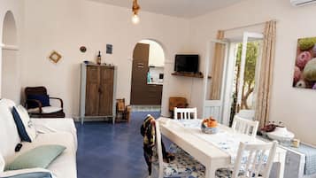 Een ruime woonkamer met een eethoek, een keuken op de achtergrond en een groot raam met gordijnen.