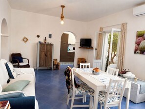 Een ruime woonkamer met een eethoek, een keuken op de achtergrond en een groot raam met gordijnen.