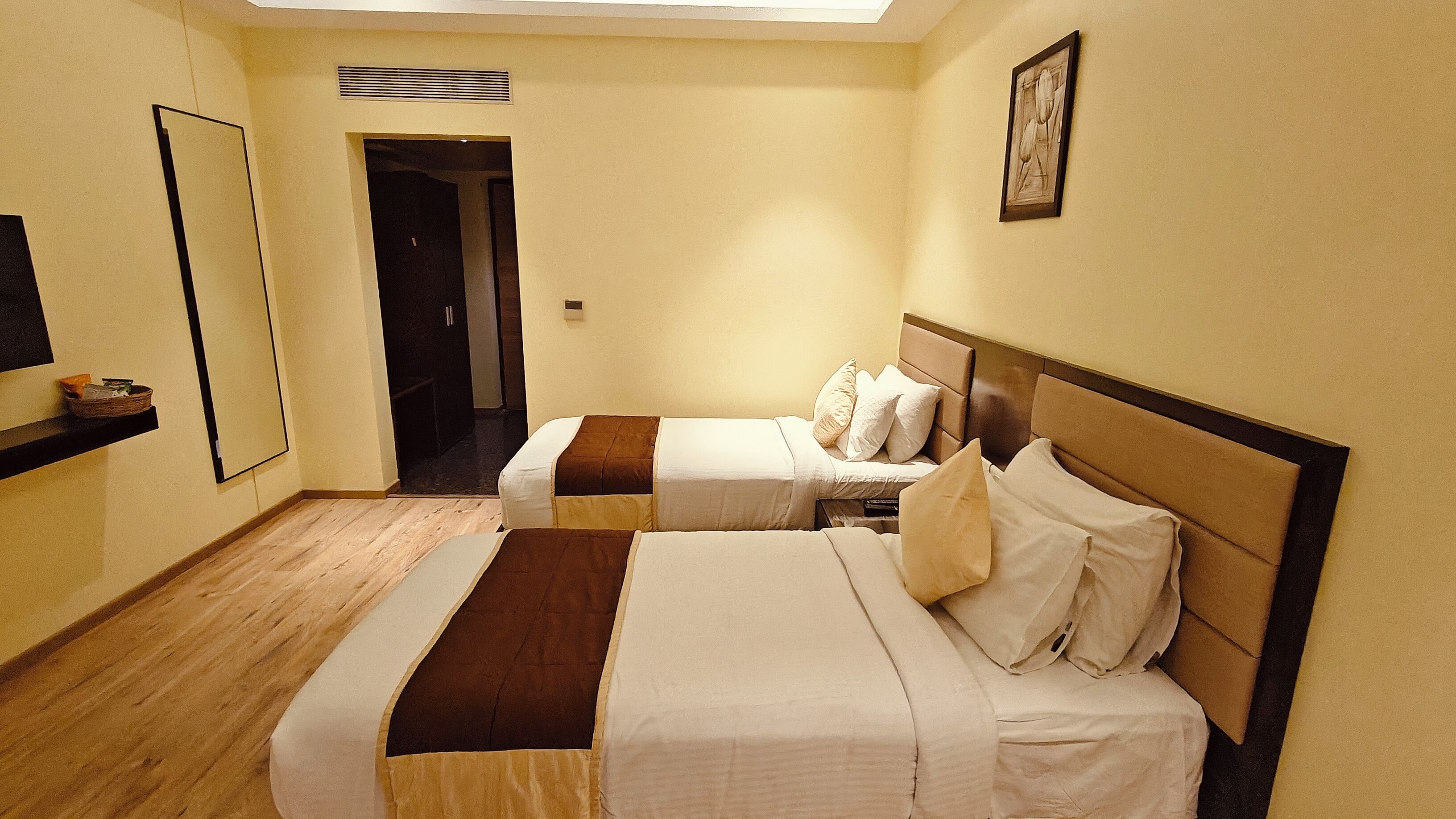 Une chambre d’hôtel avec deux lits, un grand miroir, un plancher en bois et une porte donnant sur une autre pièce.