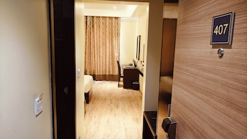 Habitación de hotel con una puerta de madera que lleva el número 407, una cama, un escritorio con una silla y un espejo en la pared.
