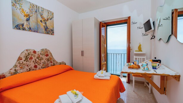 Ein Zimmer mit Bett, Tisch, Stuhl, Fernseher und Balkontür.