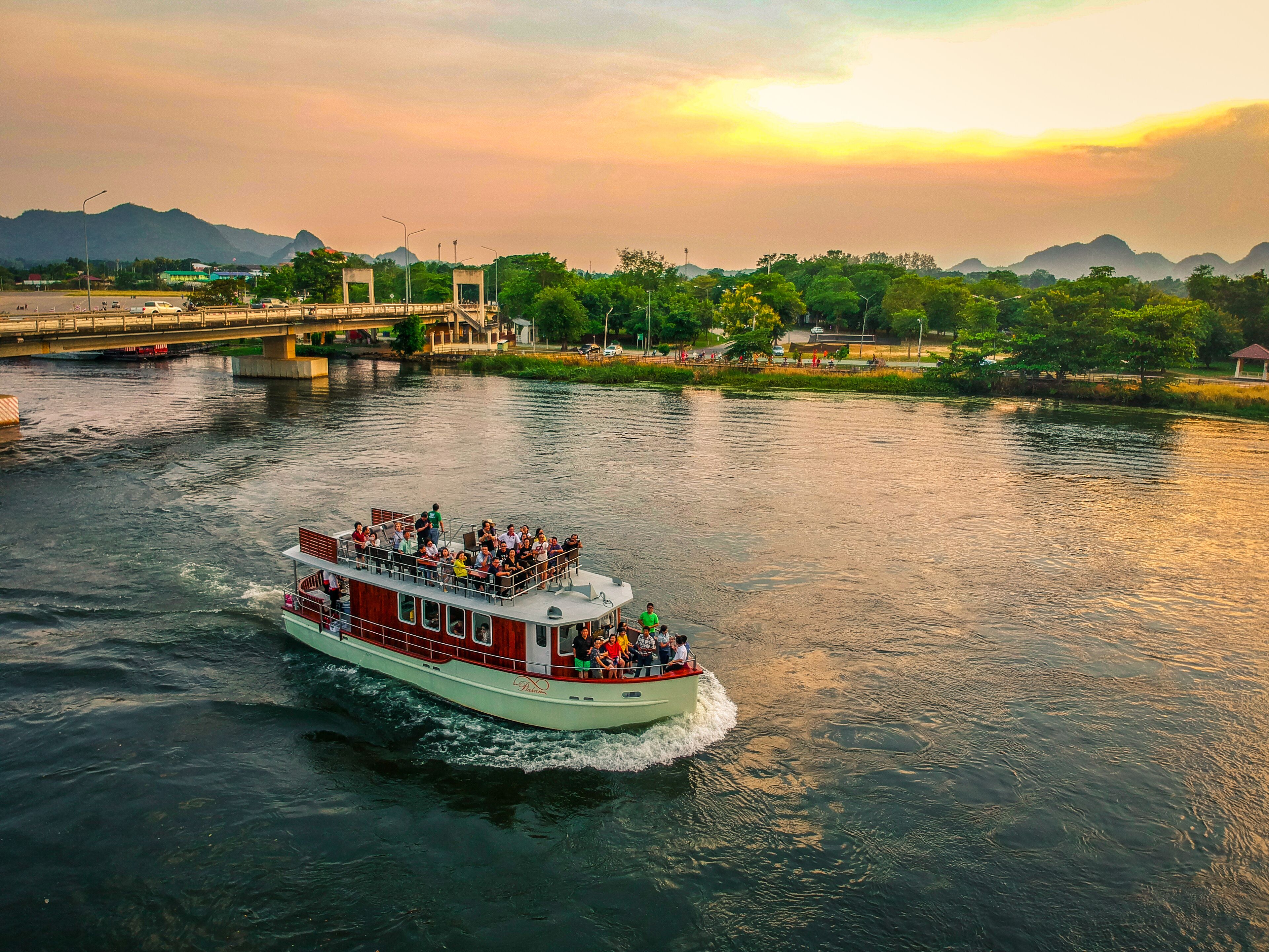 A riverboat with passengers, a bridge, and a cityscape with mountains in the background.
