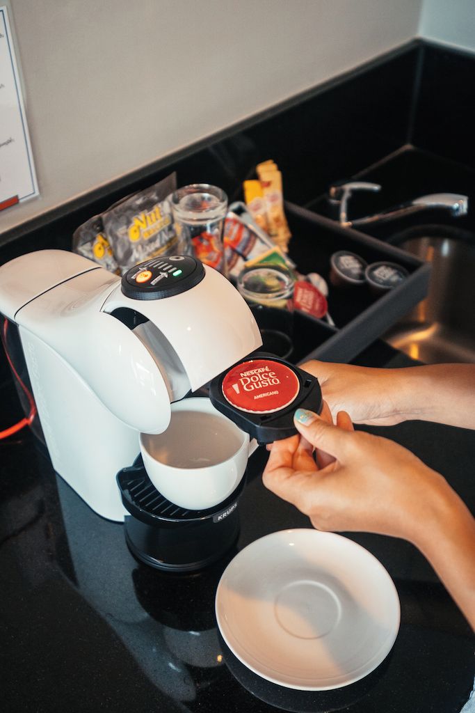 Une personne utilise une machine à café, une tasse et un bol sont posés sur le comptoir.