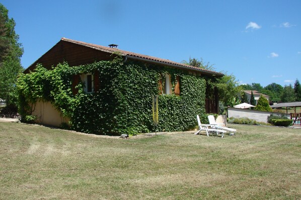 A house with a sloped roof, ivy-covered walls, and a lawn with two white lounge chairs.