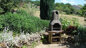 Een bakoven van natuursteen in een tuin, met veel groen en een grote boom.
