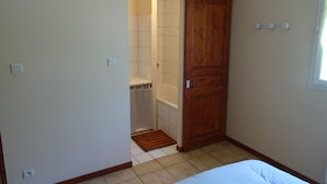Een slaapkamer met een houten garderobe, een betegelde vloer en een douchecel zichtbaar door een geopende deur.