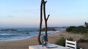 Een tafel aan het strand met een lantaarn en een glas, met op de achtergrond de oceaan en een heldere lucht.