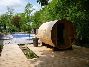 A wooden sauna structure with a door, a small outdoor seating area, and a pool in the background. - Renovated workshop for 6 people with shared, heated pool in Semur en Auxois (Semur-en-Auxois)
