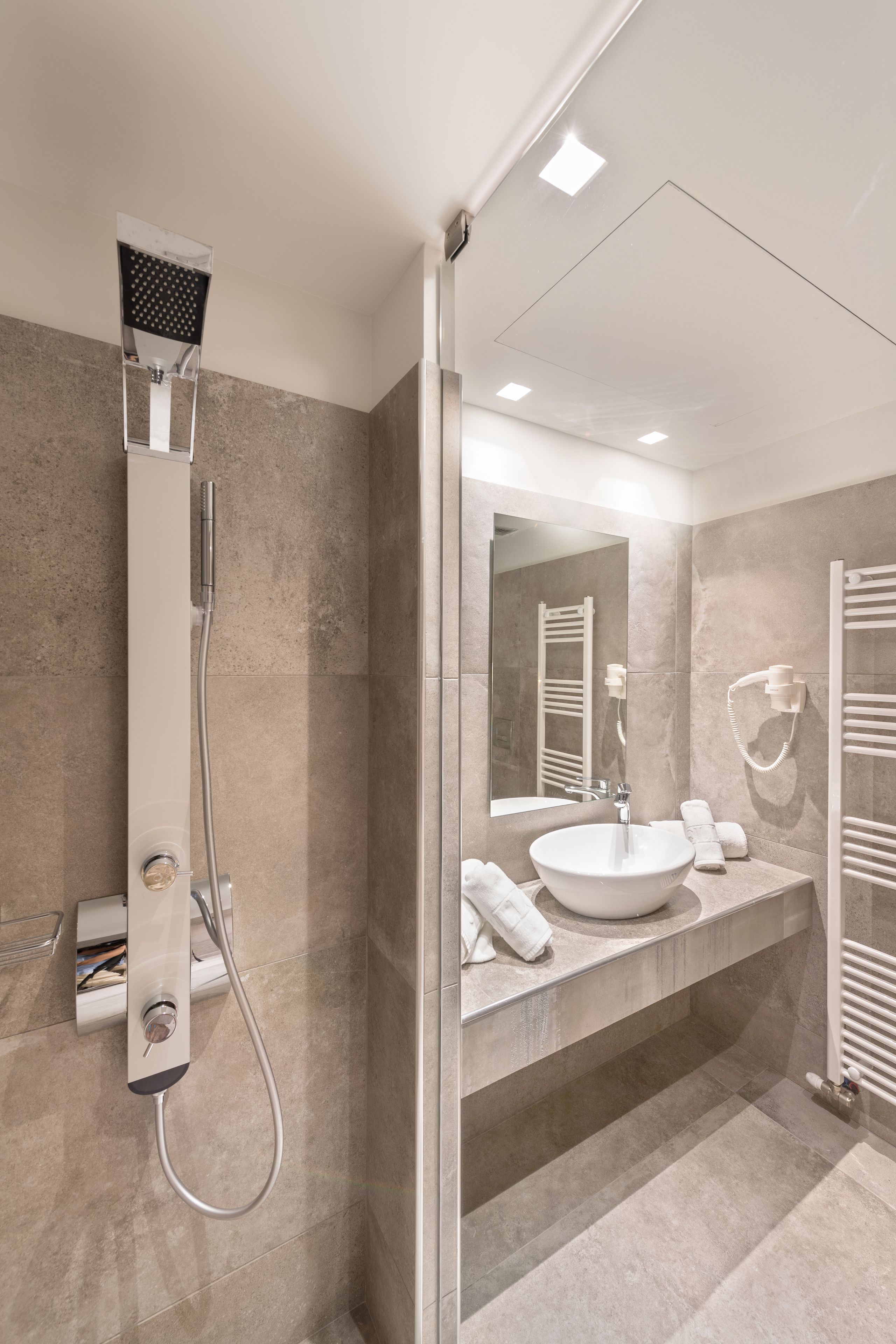 A modern bathroom with a glass shower enclosure, a large mirror, a sink with a towel rack, and a built-in heater.