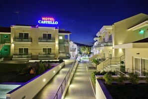 Un hotel llamado "HOTEL CASTELLO" con un estilo arquitectónico moderno, que cuenta con varios balcones y un camino central.