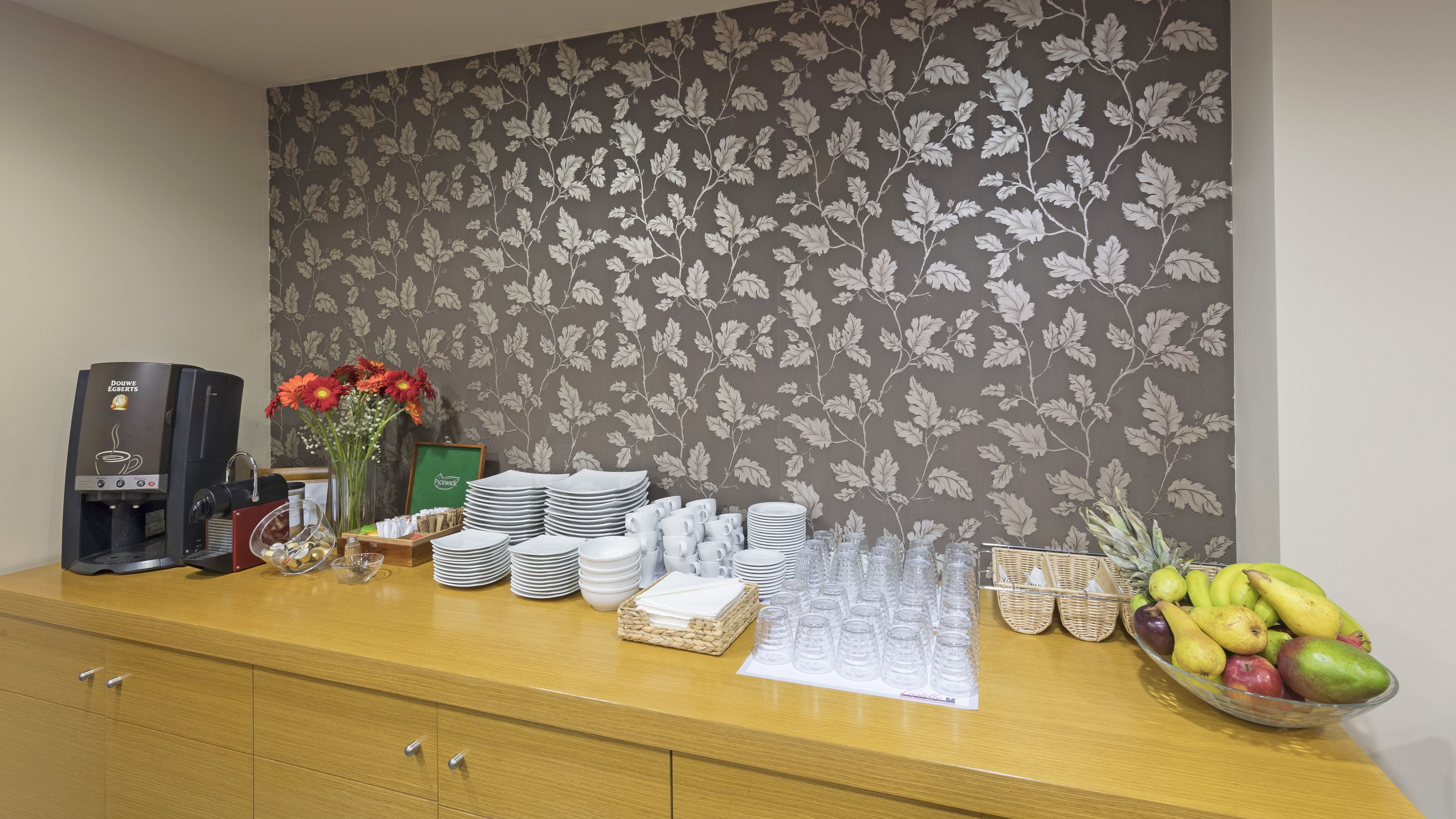 A reception area with a coffee machine, stacked plates, cups, and a fruit bowl.