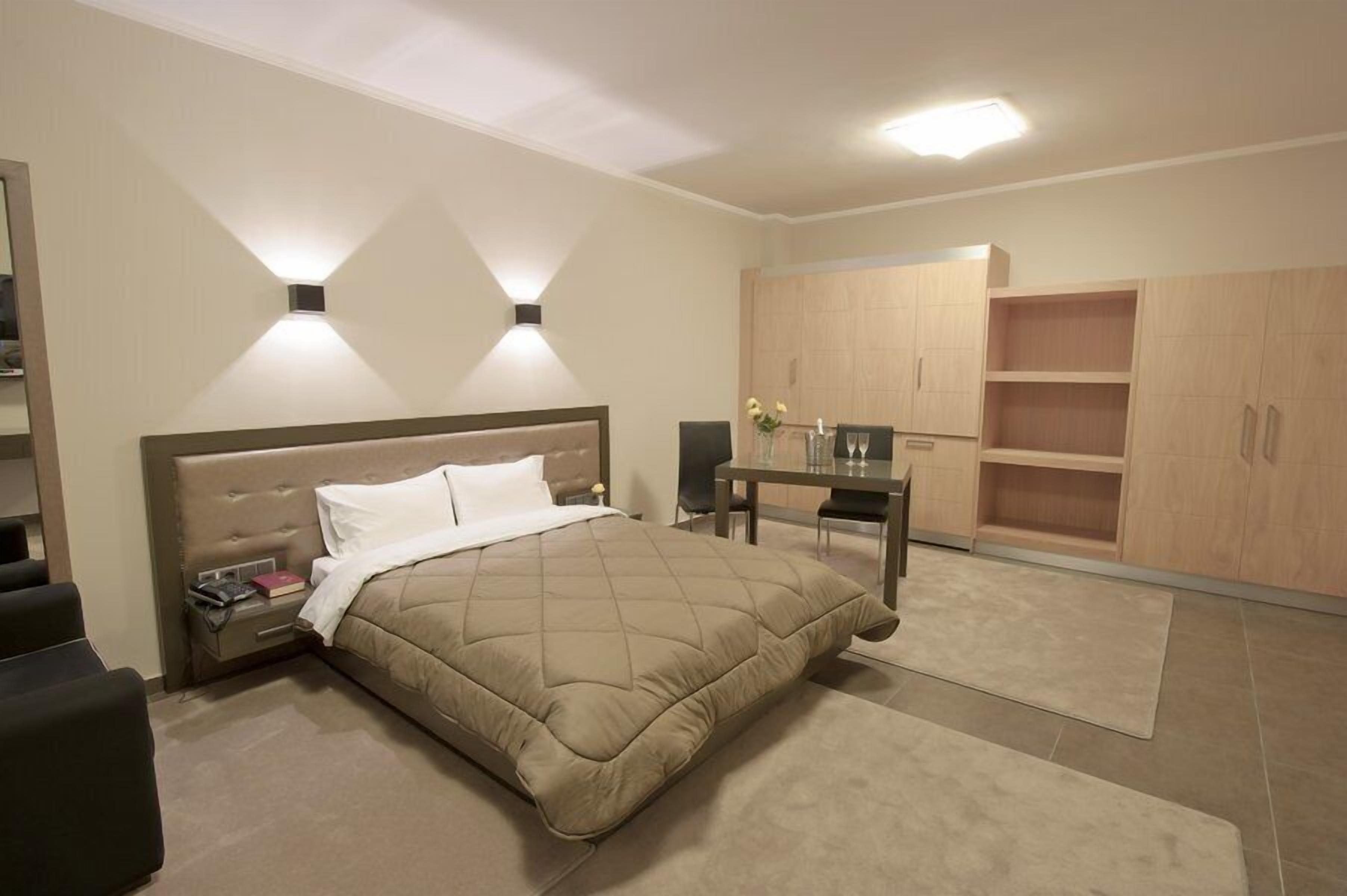 A bedroom with a bed, bedside tables, a desk, and built-in wooden cabinets.