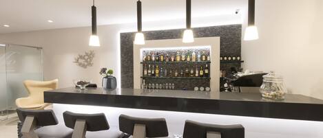 Un espace bar moderne avec un comptoir noir, trois tabourets de bar et une étagère remplie de bouteilles d’alcool.