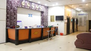 A reception area with a marble wall, a reception desk, and a sign with a blue 'H'. - Huaye Hotel (Zhuhai)