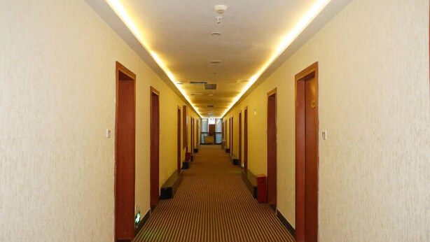 A hotel hallway with carpeted floors, wooden doors, and overhead lighting. - Huaye Hotel (Zhuhai)